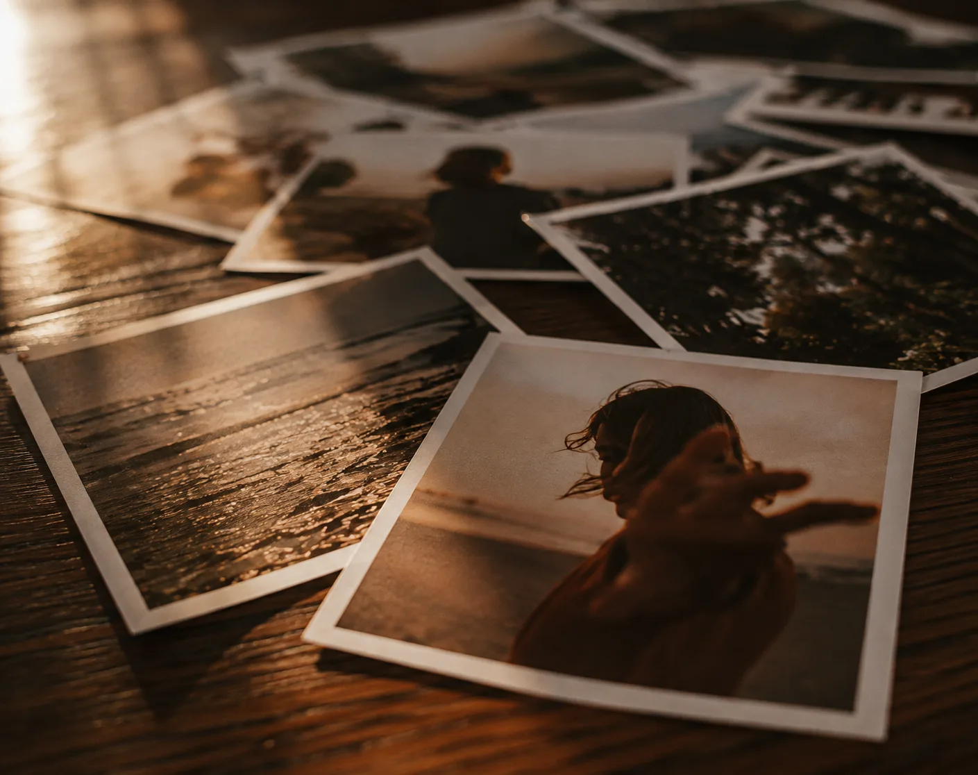A loose pile of printed photographs scattered on a warm wood table